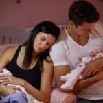 Tired Parents Cuddling Twin Baby Daughters In Nursery